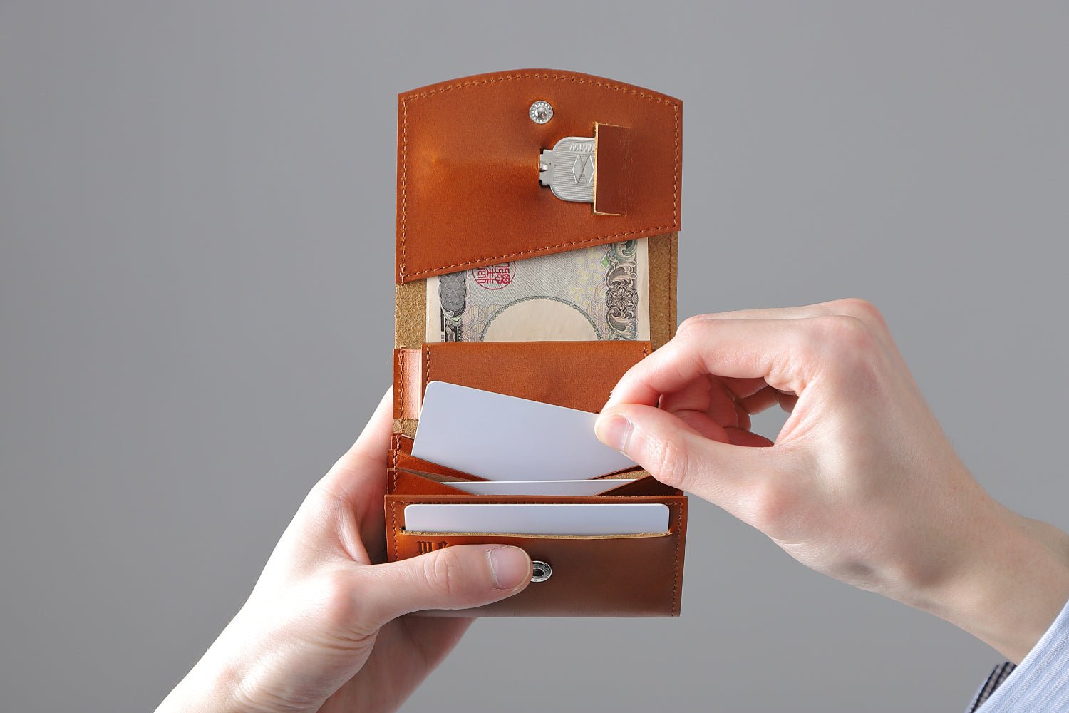 MC-bifoldwallet。蔵前の革職人が製作した国産牛革の薄いコンパクト二つ折り財布。キャメル。カードホルダーからカードを取り出しているイメージ。