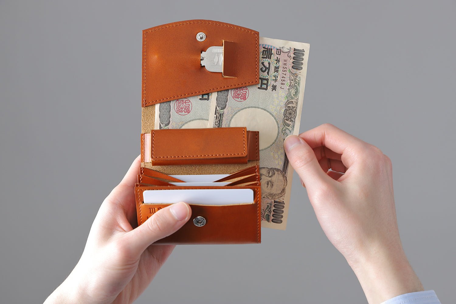 MC-bifoldwallet。蔵前の革職人が製作した国産牛革の薄いコンパクト二つ折り財布。キャメル。紙幣を取り出しているイメージ。