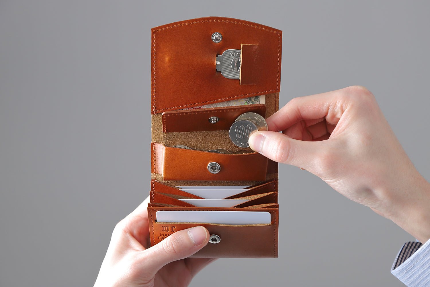 MC-bifoldwallet。蔵前の革職人が製作した国産牛革の薄いコンパクト二つ折り財布。キャメル。小銭を取り出しているイメージ。