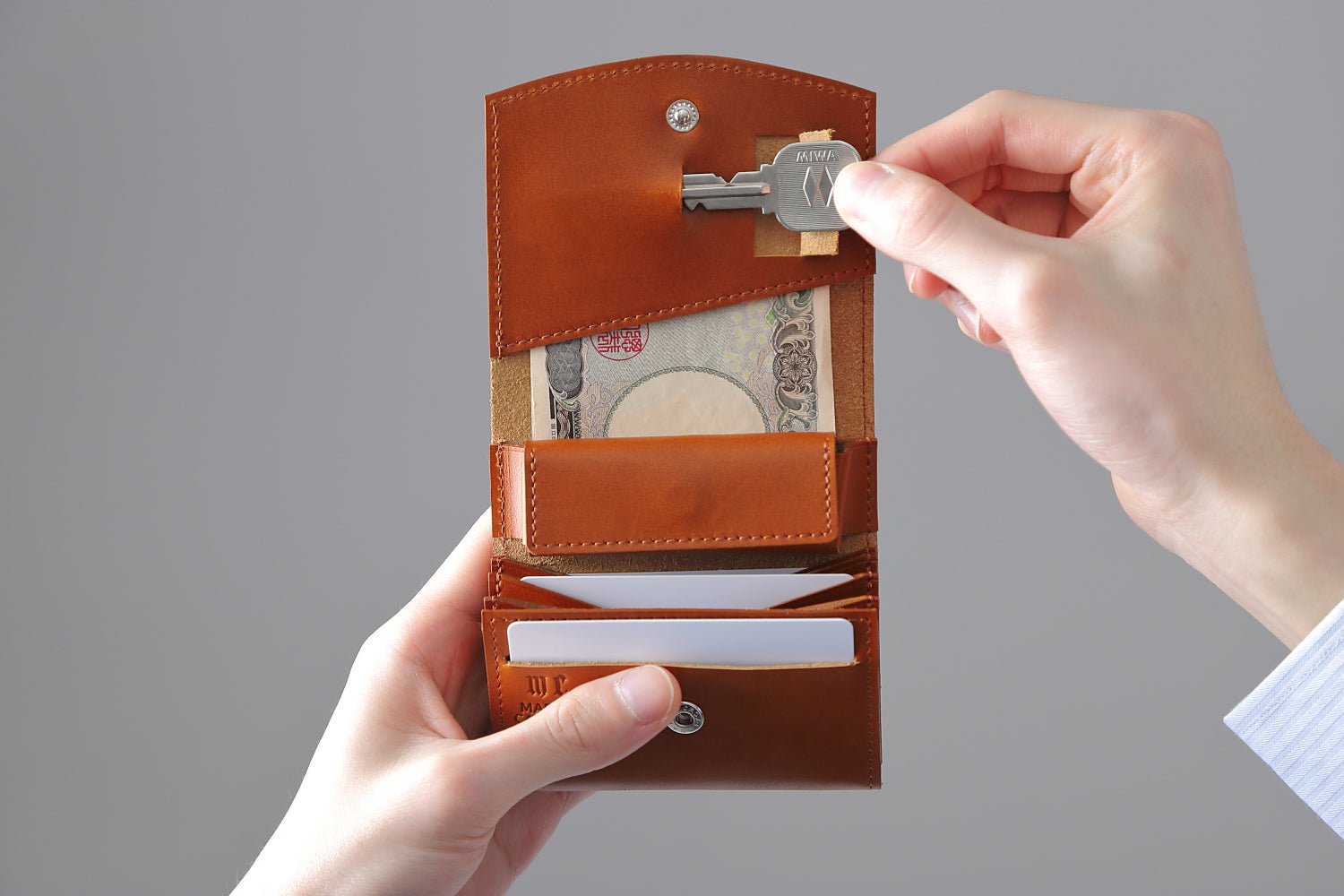 MC-bifoldwallet。蔵前の革職人が製作した国産牛革の薄いコンパクト二つ折り財布。キャメル。鍵を取り出しているイメージ。