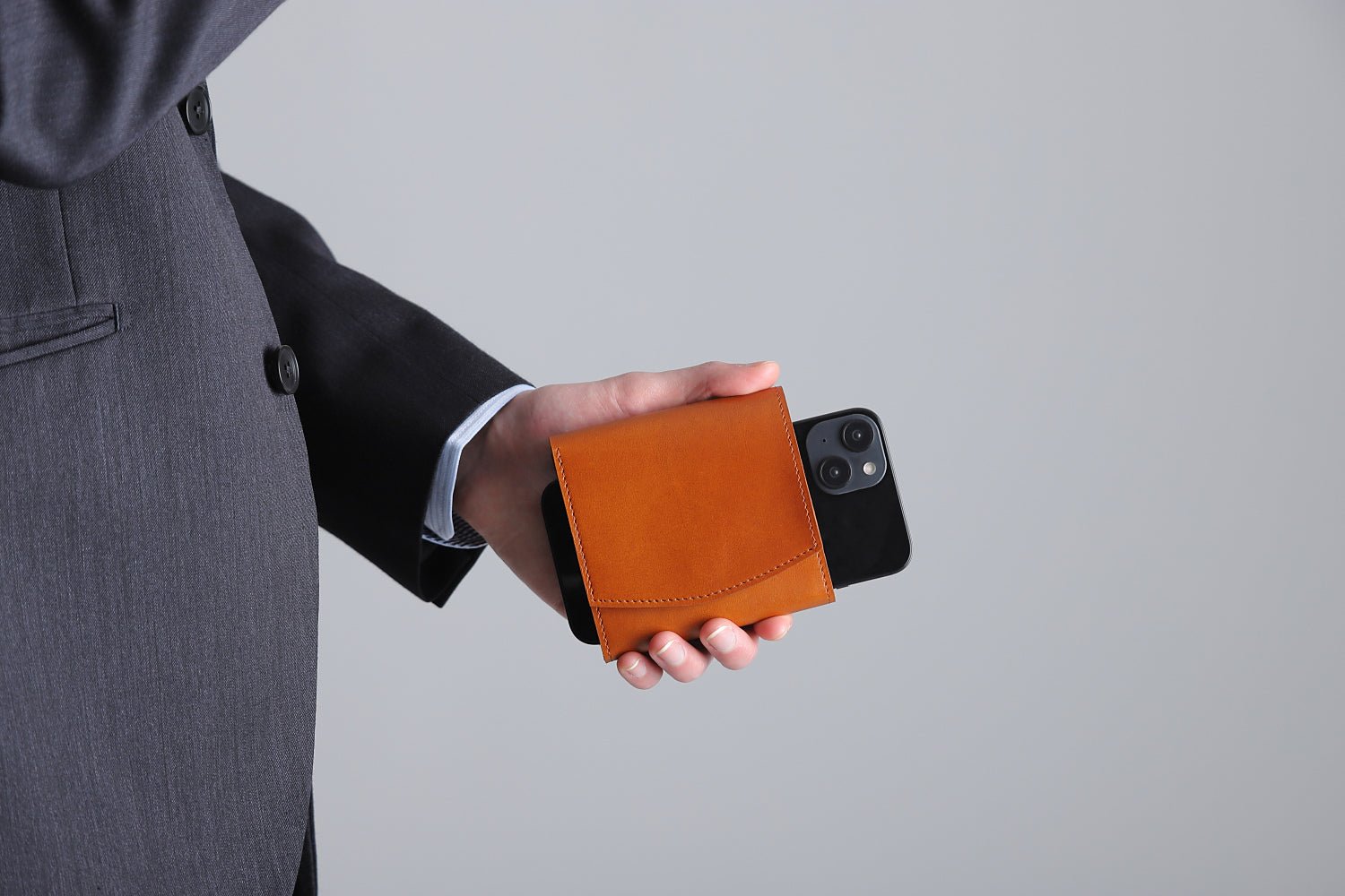 MC-bifoldwallet。蔵前の革職人が製作した国産牛革の薄いコンパクト二つ折り財布。キャメル。財布とスマホを持ち合わせしているシーン。