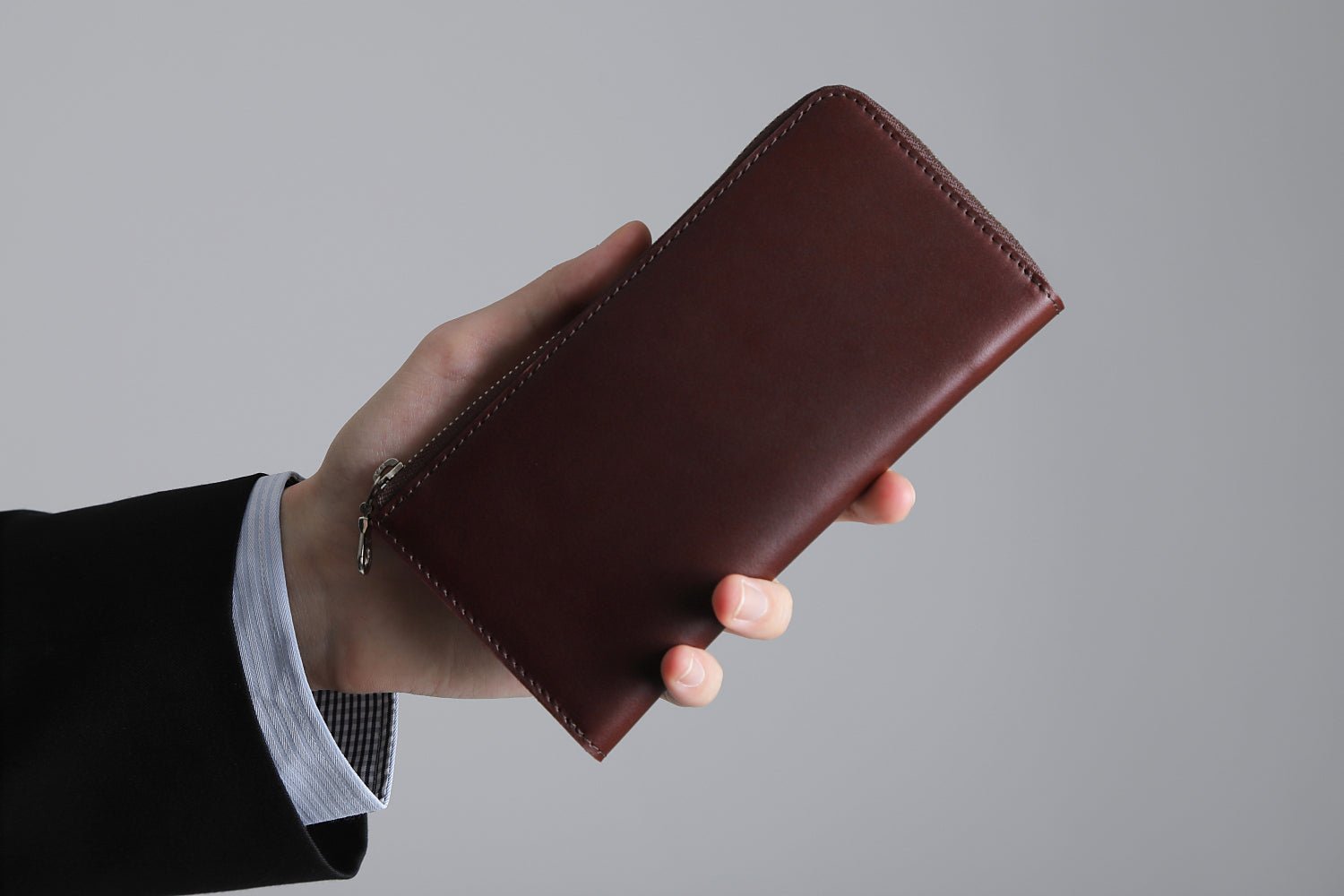 MC-longwallet。蔵前の革職人が製作した国産牛革のL字ファスナーコンパクト長財布。バーガンディ。財布を手に持ってるシーン。