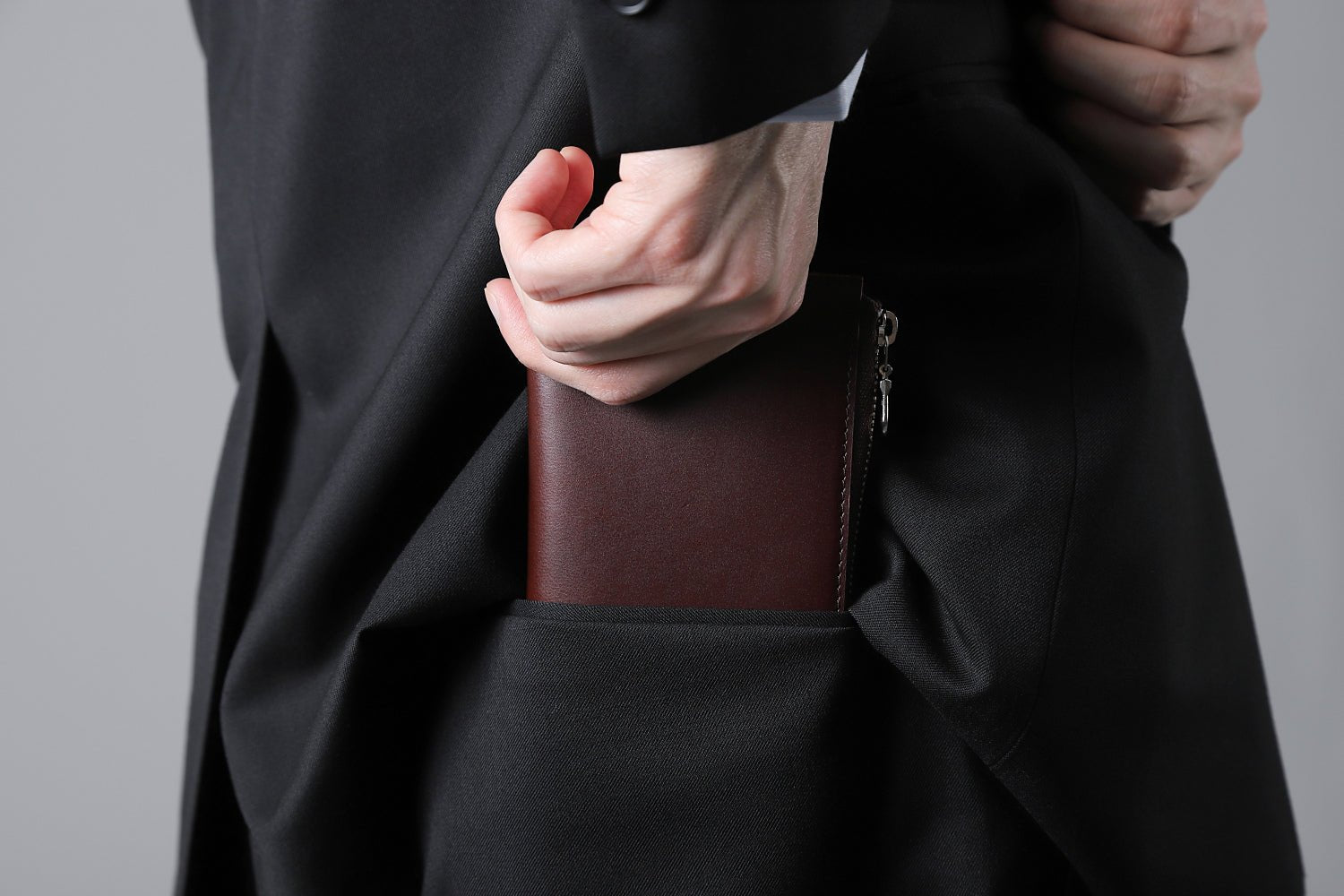 MC-longwallet。蔵前の革職人が製作した国産牛革のL字ファスナーコンパクト長財布。バーガンディ。財布を後ろポケットにしまうシーン。