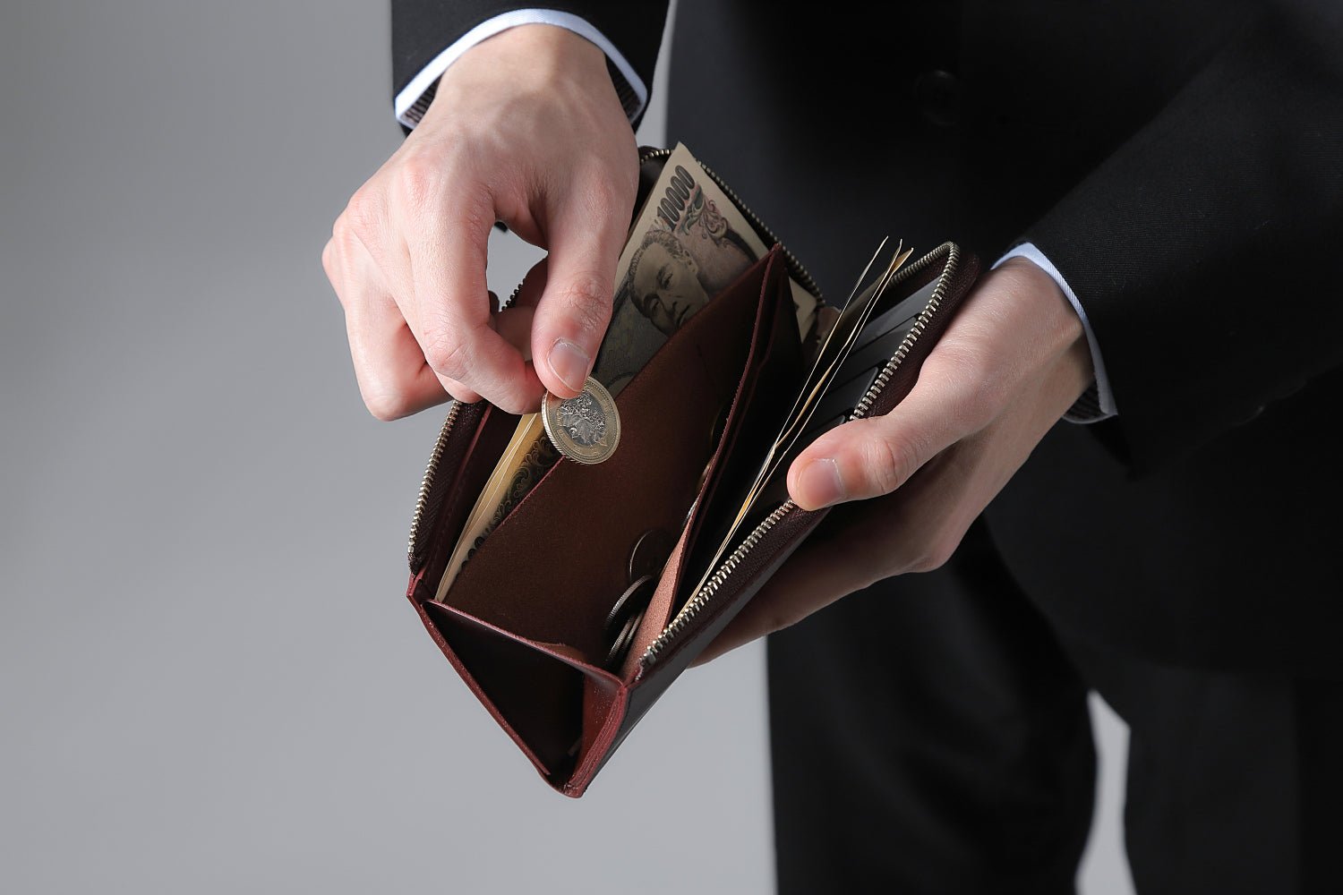 MC-longwallet。蔵前の革職人が製作した国産牛革のL字ファスナーコンパクト長財布。バーガンディ。小銭を取り出しているイメージ。