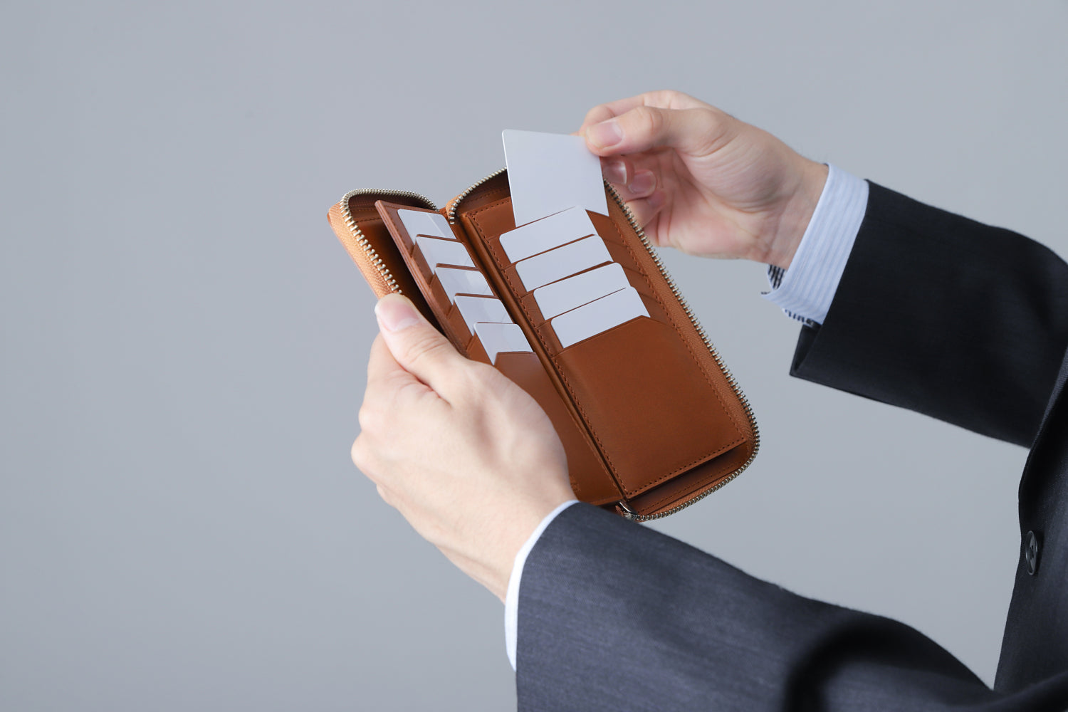MC-longwallet2。蔵前の革職人が製作した国産牛革のラウンドファスナーコンパクト長財布。キャメル。カードホルダーからカードを取り出しているイメージ。