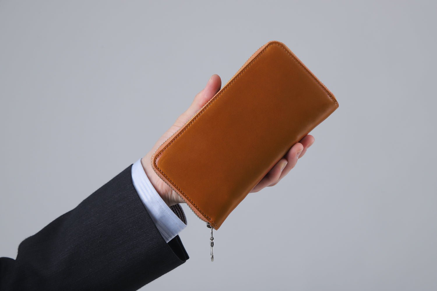 MC-longwallet2。蔵前の革職人が製作した国産牛革のラウンドファスナーコンパクト長財布。キャメル。財布を手に持ってるシーン。