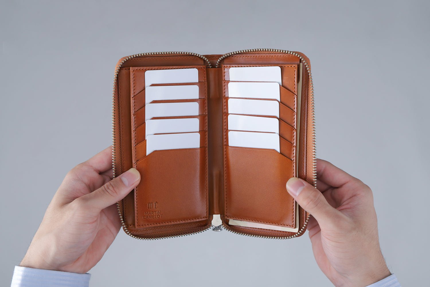 MC-longwallet2。蔵前の革職人が製作した国産牛革のラウンドファスナーコンパクト長財布。キャメル。カードを収納し、手で財布を見開いているシーン。