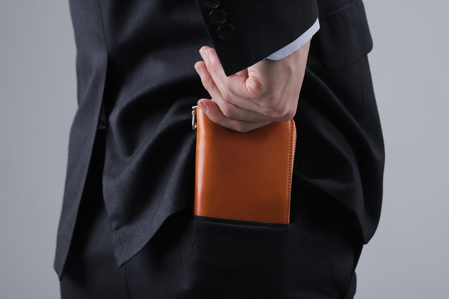 MC-longwallet2。蔵前の革職人が製作した国産牛革のラウンドファスナーコンパクト長財布。キャメル。財布を後ろポケットにしまうシーン。