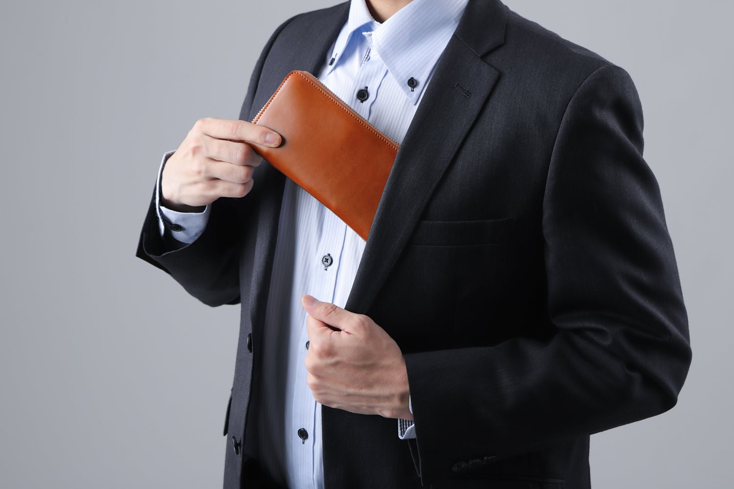 MC-longwallet2。蔵前の革職人が製作した国産牛革のラウンドファスナーコンパクト長財布。キャメル。財布を胸ポケットにしまうシーン。
