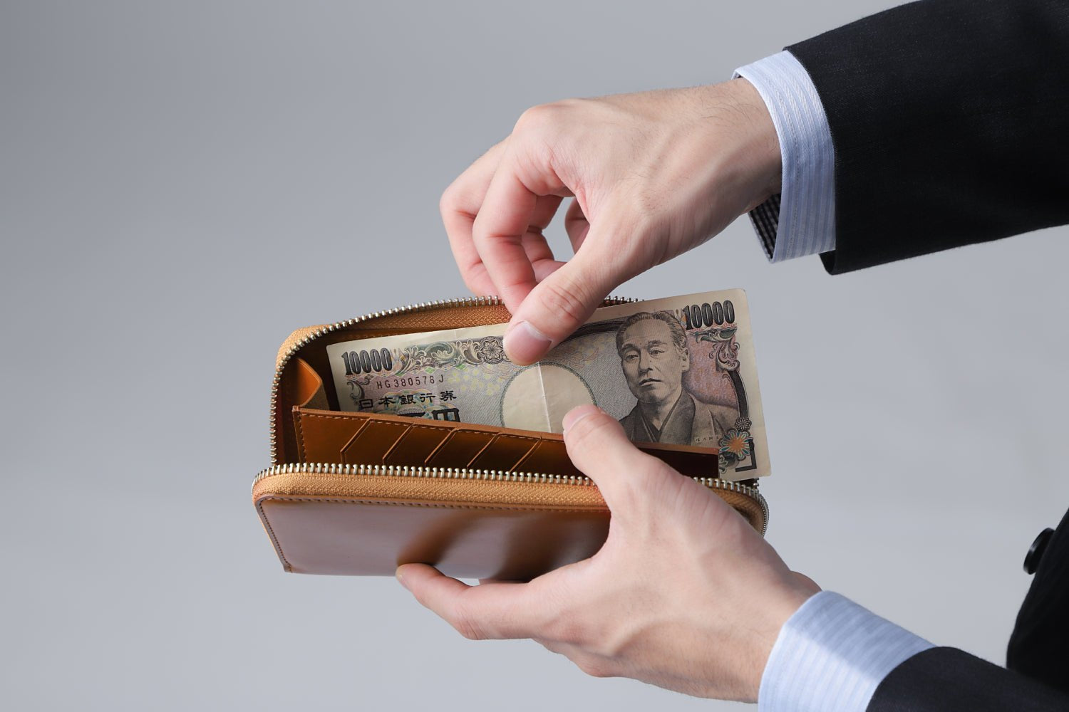 MC-longwallet2。蔵前の革職人が製作した国産牛革のラウンドファスナーコンパクト長財布。キャメル。紙幣を取り出しているイメージ。