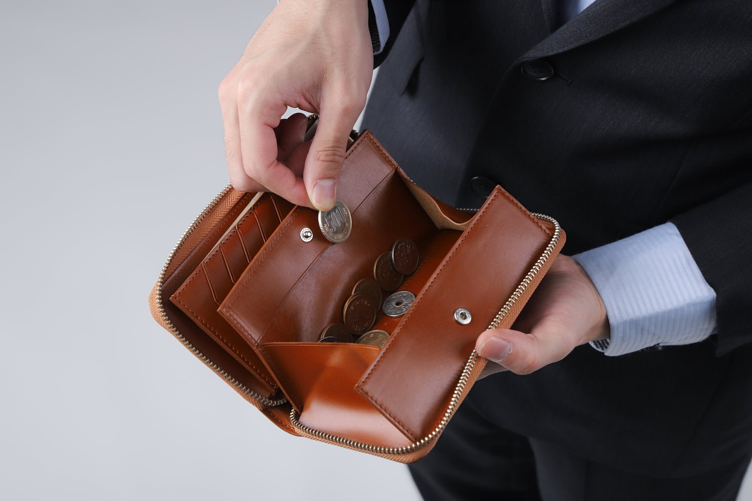 MC-longwallet2。蔵前の革職人が製作した国産牛革のラウンドファスナーコンパクト長財布。キャメル。小銭を取り出しているイメージ。
