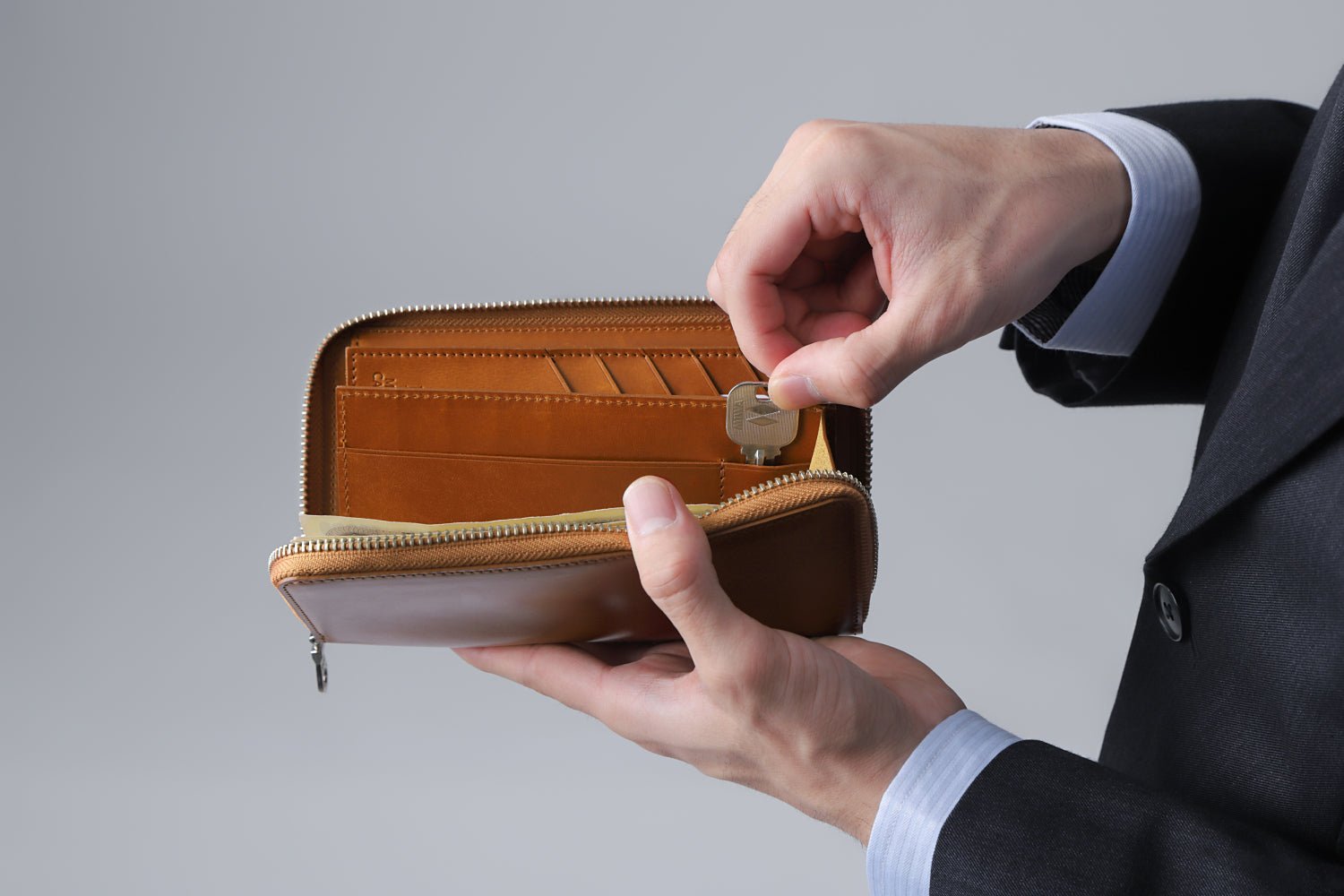 MC-longwallet2。蔵前の革職人が製作した国産牛革のラウンドファスナーコンパクト長財布。キャメル。鍵を取り出しているイメージ。