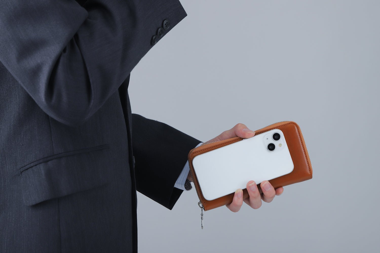 MC-longwallet2。蔵前の革職人が製作した国産牛革のラウンドファスナーコンパクト長財布。キャメル。財布とスマホを持ち合わせしているシーン。