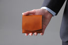 0MC-bifoldwallet。蔵前の革職人が製作した国産牛革の蛇腹式コンパクト二つ折り財布。キャメル。財布を手に持ってるシーン。