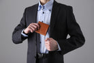 MC-bifoldwallet。蔵前の革職人が製作した国産牛革の蛇腹式コンパクト二つ折り財布。キャメル。財布を胸ポケットにしまうシーン。