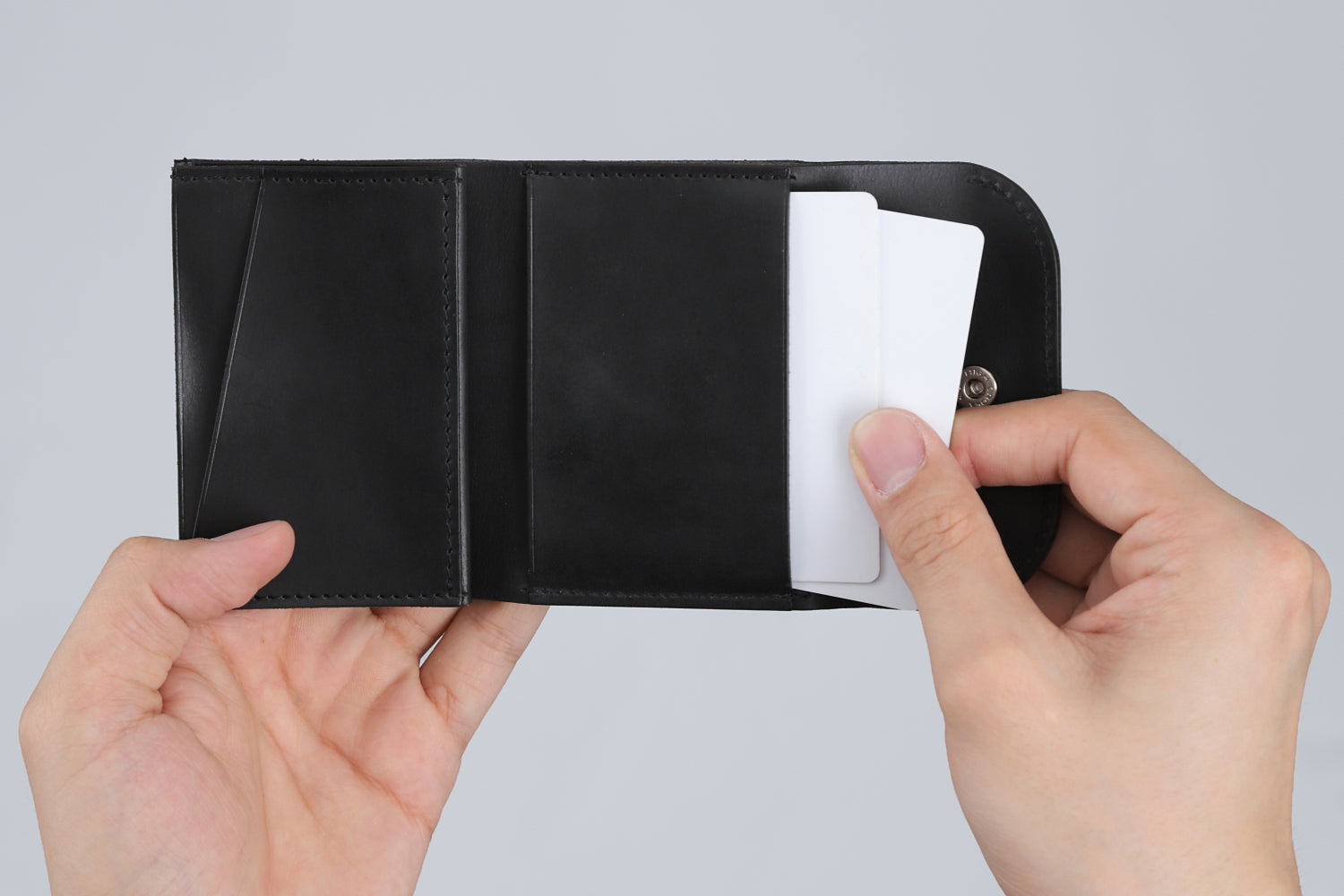 MC-compactwallet。蔵前の革職人が製作した国産牛革のコンパクト財布。ブラック。中央ポケットからカードを取り出しているイメージ。
