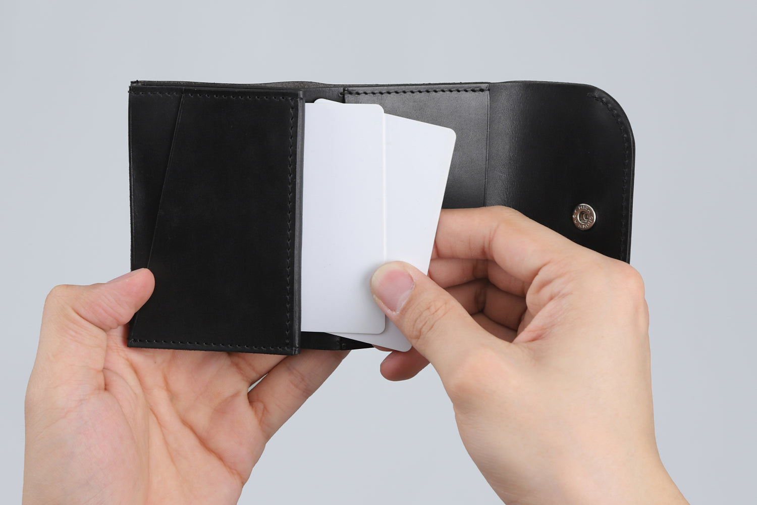 MC-compactwallet。蔵前の革職人が製作した国産牛革のコンパクト財布。ブラック。左側ポケットからカードを取り出しているイメージ。