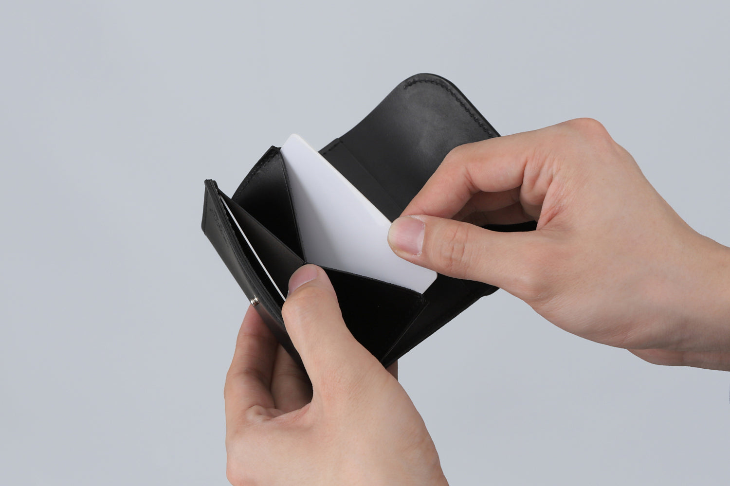 MC-compactwallet。蔵前の革職人が製作した国産牛革のコンパクト財布。ブラック。カードホルダーからカードを取り出しているイメージ。