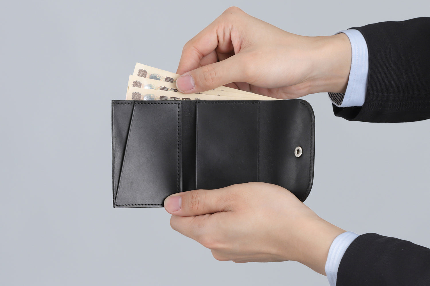 MC-compactwallet。蔵前の革職人が製作した国産牛革のコンパクト財布。ブラック。紙幣を取り出しているイメージ。