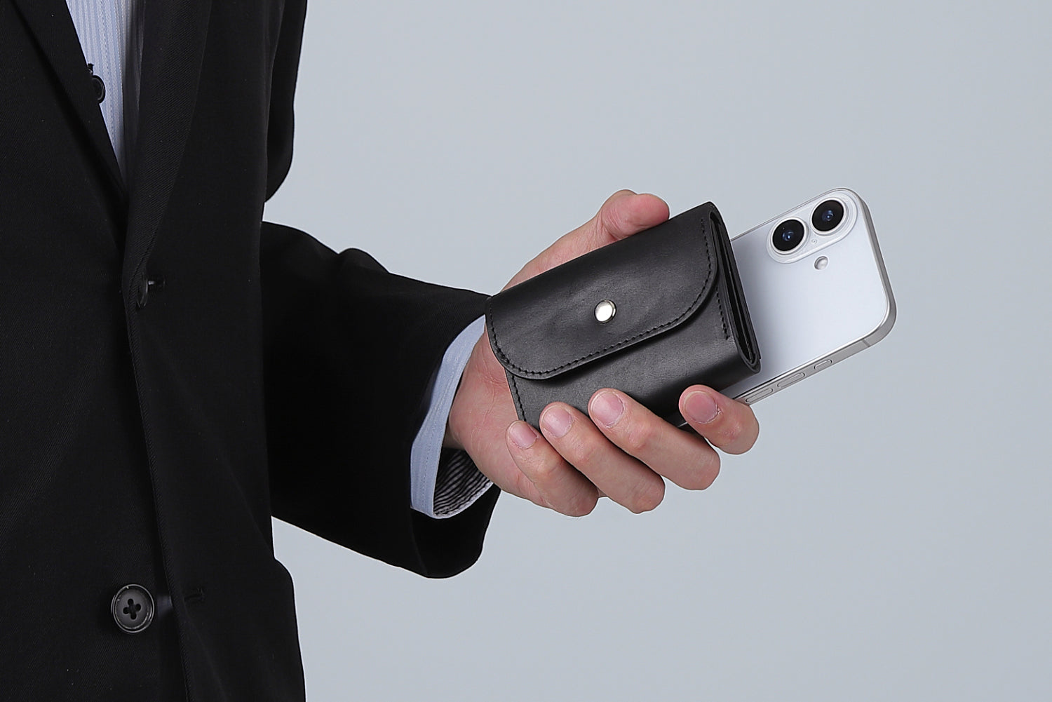 MC-compactwallet。蔵前の革職人が製作した国産牛革のコンパクト財布。ブラック。財布とスマホを持ち合わせしているシーン。