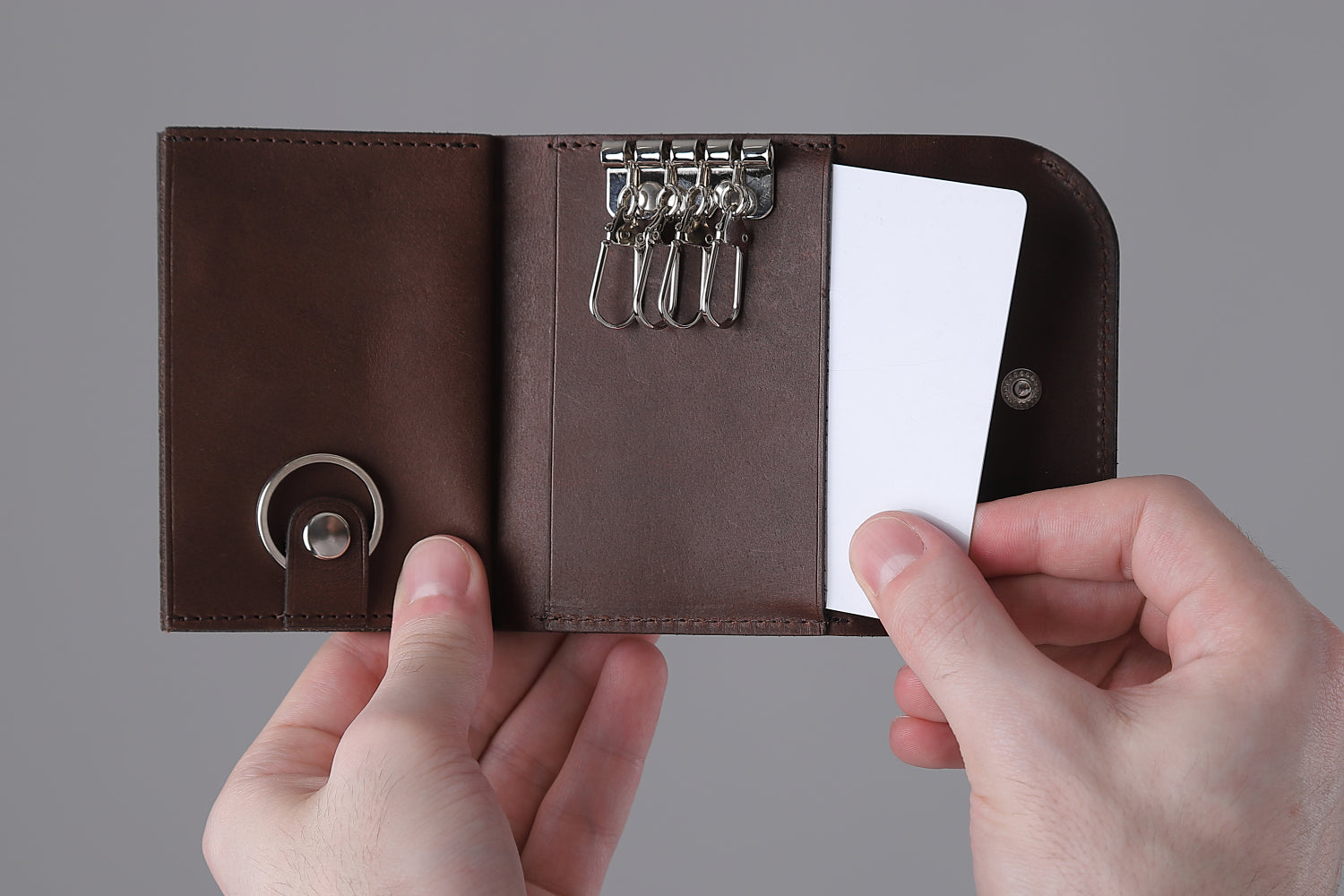 MC-keyminimal。蔵前の革職人が製作した国産牛革のキーケース一体型ミニマル財布。ダークブラウン。中央ポケットからカードを取り出しているイメージ。