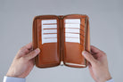 MC-longwallet2。蔵前の革職人が製作した国産牛革のラウンドファスナーミニマル長財布。キャメル。カードを収納し、手で財布を見開いているシーン。